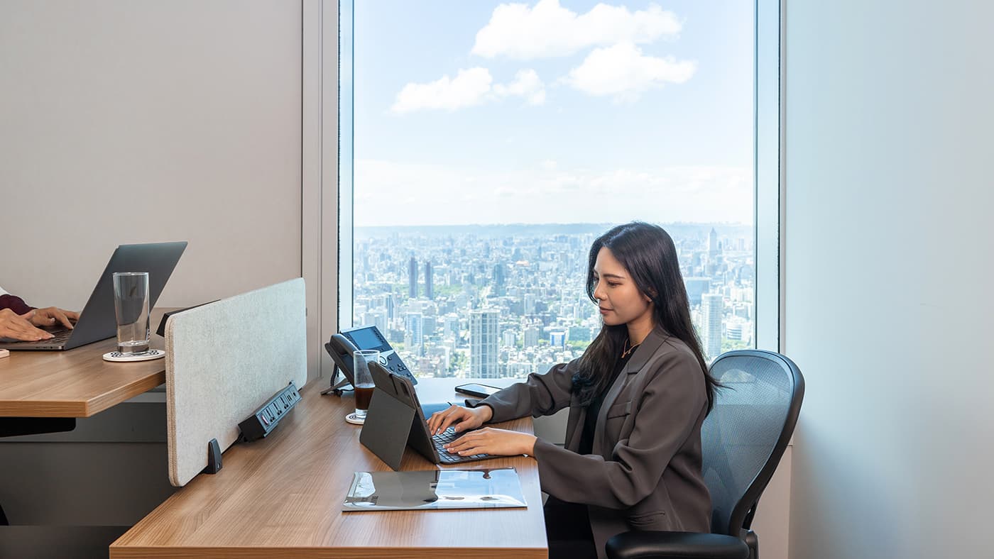 有人在办公室里用笔记本电脑工作,背景是台北城市景观