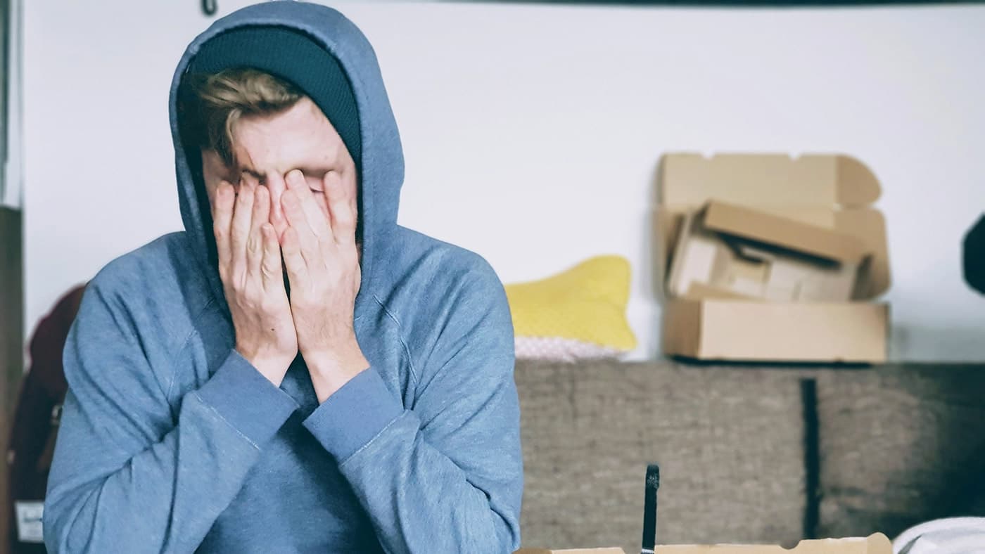 一名穿着连帽衫的男子坐在桌子旁因为过劳而感到苦恼